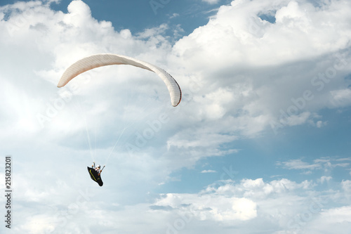 Professional paraglider flies on a white paraglider against the blue sky and white clouds. Paragliding sport