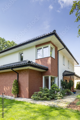 House with red brick wall with green grass and garden under sky