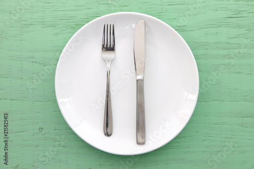 緑の木製テーブルに置かれた白い皿とカトラリーによる食事終了の合図