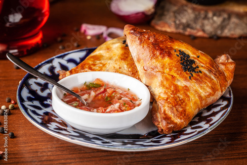 Uzbek samsa in national plate with tomato sauce on a wooden table. end of the eastern baking. photo