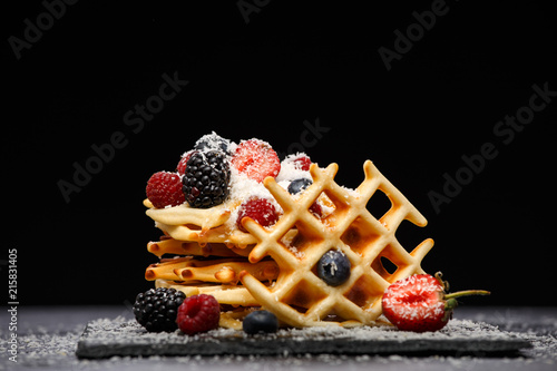 Photo of viennese wafers with fresh raspberries, strawberries sprinkled with powdered sugar on blackboard against blank background