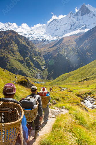 Porters carrying doko baskets from Annapurna Base camp down valley toward Machapuchare in the Annapurna Himalaya, Nepal.
