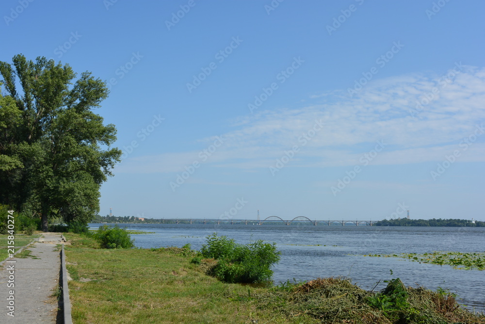 Сity landscape with green trees on the left bank of the city, river and new houses on the second shore and white clouds above them