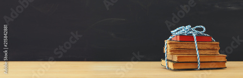 back to school concept. stack of books over wooden desk in front of blackboard.