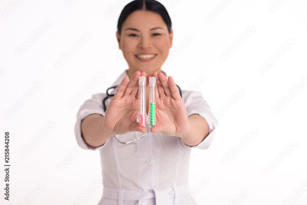 Gorgeous smiling nurse with medicine in her hands. Asian female medical doctor with two thin bottles of coloured pills holding them close to camera. Gorgeous smiling nurse with medicine in her hands. Asian female medical doctor with two thin bottles of coloured pills holding them close to camera.