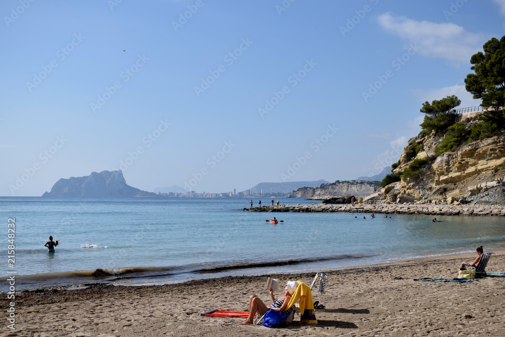 A lady lying on a sunbed and reading book enjoying a vacation on a magnificent sandy beach in Spain