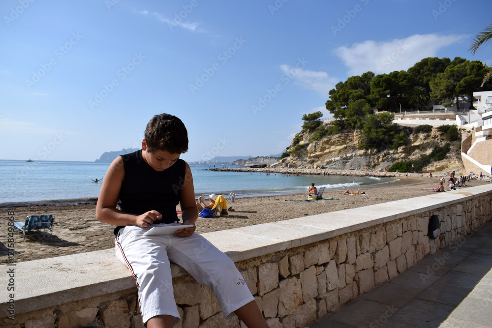 A boy playing games on a tablet on a bench
