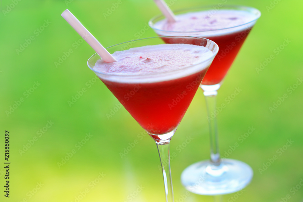 Two martini shape glasses with straws filled with red chilled drink on green background Two martini shape glasses with straws filled with red chilled drink on green background