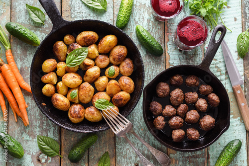 Scandinavian cuisine. Fried potatoes, meatballs and lingonberry drink served with vegetables and herbs on rustic blue table