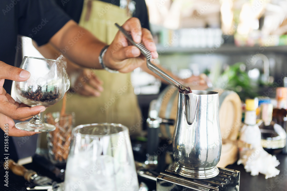 The bartender put the spice in the kettle to get ready for the beverage. The bartender put the spice in the kettle to get ready for the beverage.