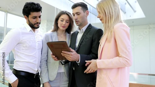 Business Partners Discussing their Business Ideas, Future Projects. Standing at the Glass Hall. Huge Modern Office. Collegues Discussing Together. Typing on Digital Tablet. Classically Dressed. photo