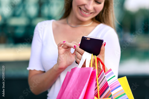 Cheerful girl with a phone and shopping bags at the mall. Quickly and easily make an order online, pay, get a profitable offer