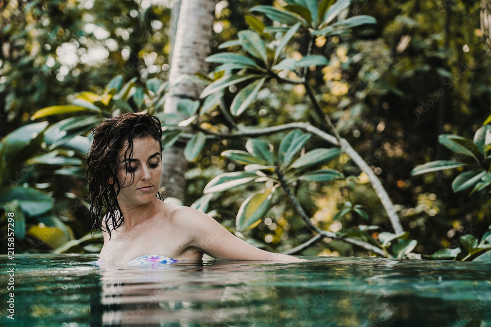 Fototapeta premium .Young and pretty woman enjoying her vacation in Ubud, in the Bali island, Indonesia. A summer afternoon in the pool with a tropical background. Relaxed and happy attitude. Lifestyle.