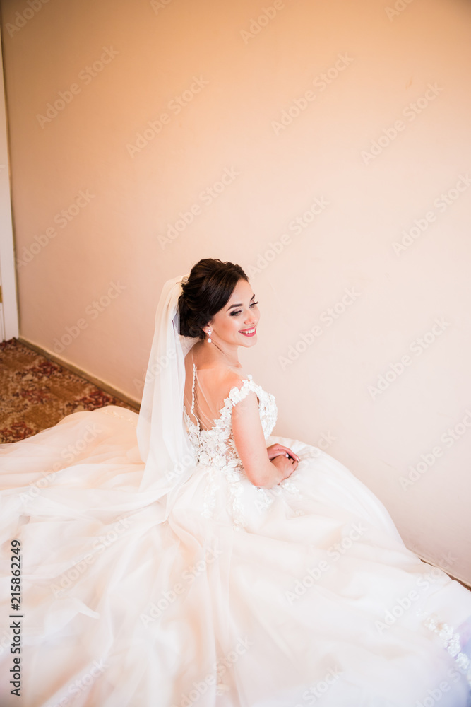 A charming bride in a white dress sitting on a bed with a flower in her hand A charming bride in a white dress sitting on a bed with a flower in her hand