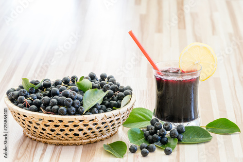 Fresh juice of chokeberry or Aronia melanocarpa in glass and berry in pot on wooden background