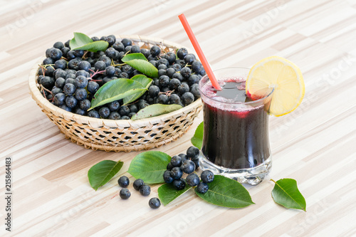 Fresh juice of chokeberry or Aronia melanocarpa in glass and berry in pot on wooden background
