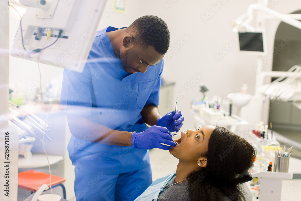 Male african dentist examining a patient with tools in dental clinic.High angle view of female