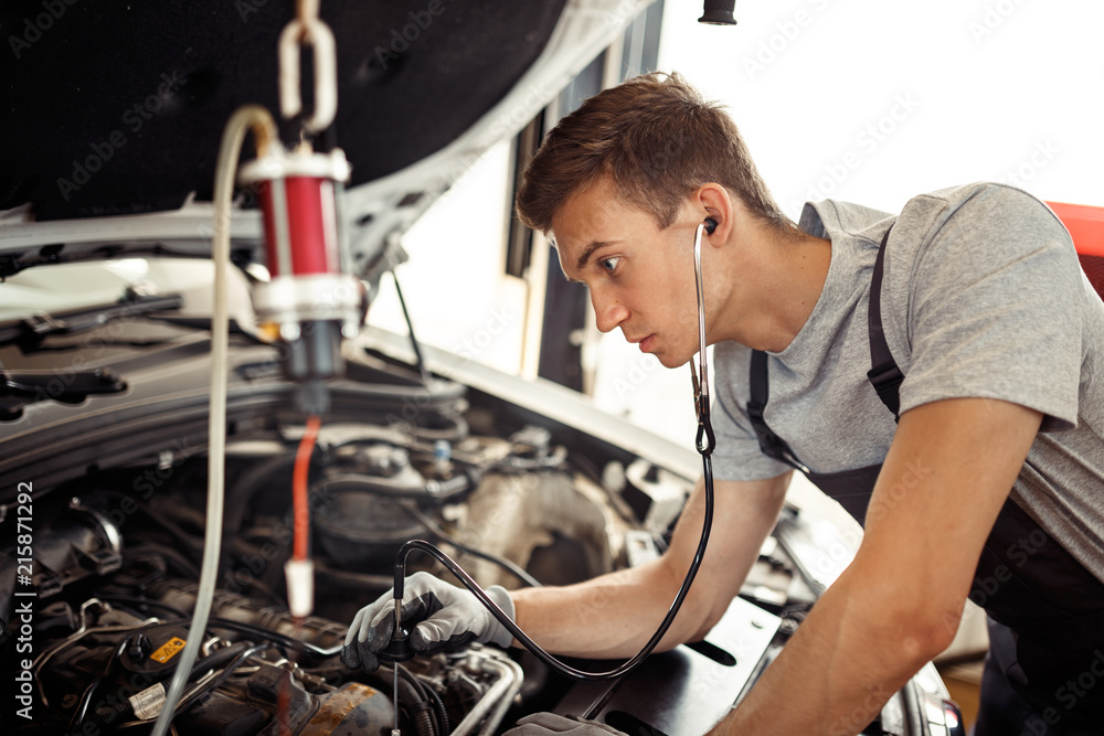 A young qualified mechanic is looking for bugs being at work at a car service