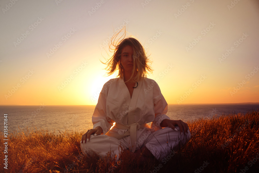 Silhouette of a girl in a kimono on the beach, Sitting in a Lotus position on the background of sunrise. The concept of meditation.