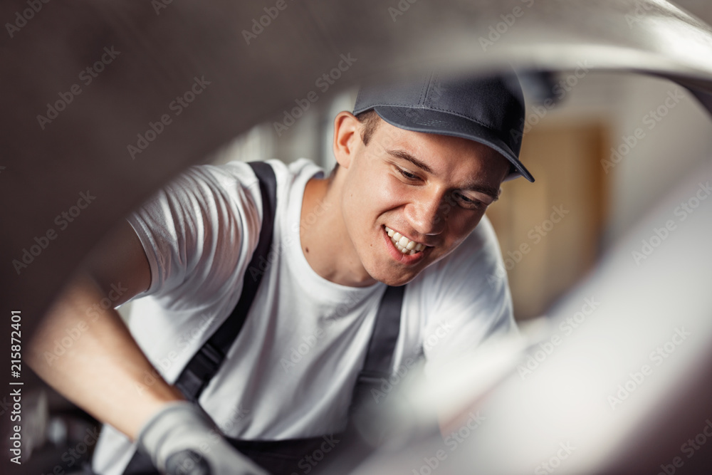 A young man is repairing a car while at work at a vehicle service A young man is repairing a car while at work at a vehicle service