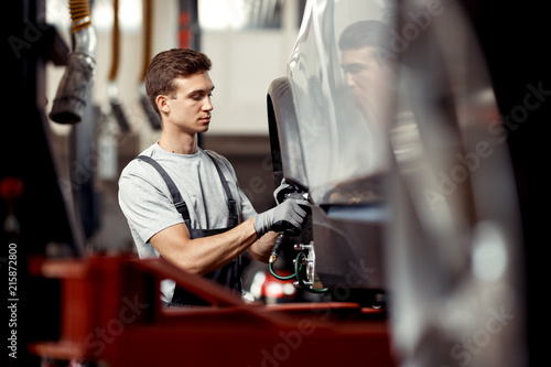 A good-looking mechanic is focused on repairing a light-gray car