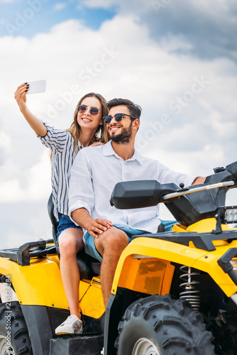 smiling young couple taking selfie while sitting on ATV