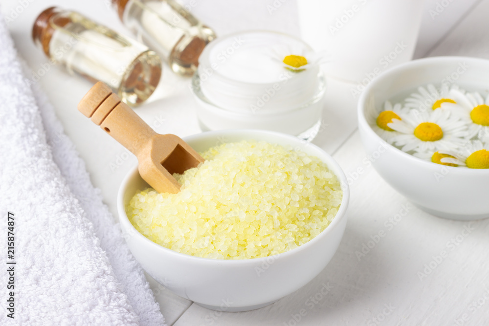 Spa background with bath yellow sea salt, natural cream and chamomile on white wooden table Spa background with bath yellow sea salt, natural cream and chamomile on white wooden table