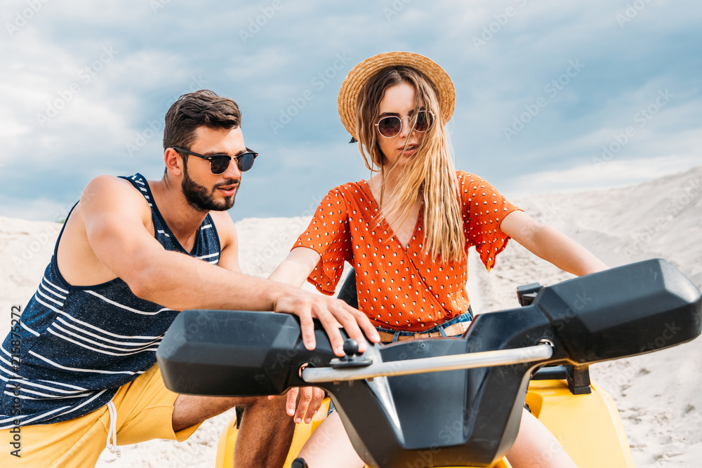 Fototapeta premium handsome young man teaching his girlfriend how to ride atv in desert
