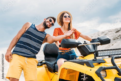 smiling young man teaching his girlfriend how to ride atv in desert