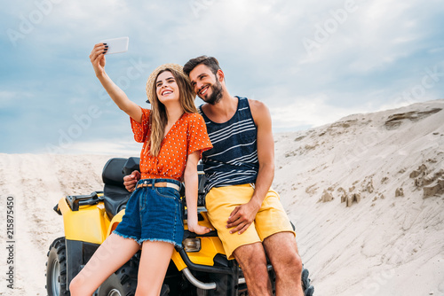 happy young couple with ATV taking selfie in desert