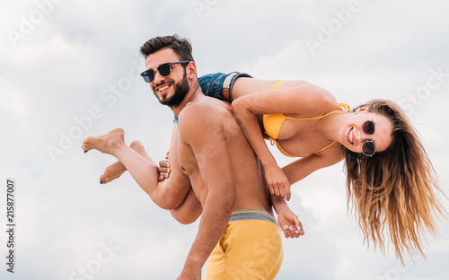 happy young man carrying his girlfriend on shoulder and looking at camera photo