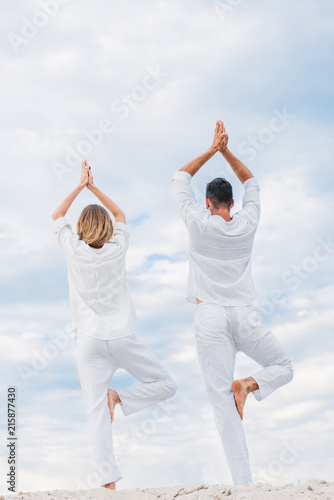 rear view of couple practicing yoga in tree pose  Vrksasana  on sandy dune