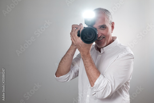 Studio shot of ymature spanish man with camera against grey background. Experienced photographer in photo studio