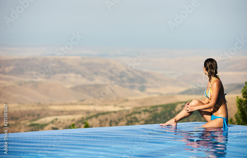 Young Woman relaxing in infinity swimming pool looking at mountain landscape view