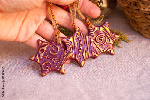 Handmade christmas ornaments from polymer clay in woman hand. Xmas card background. Claret gold decorations stars.