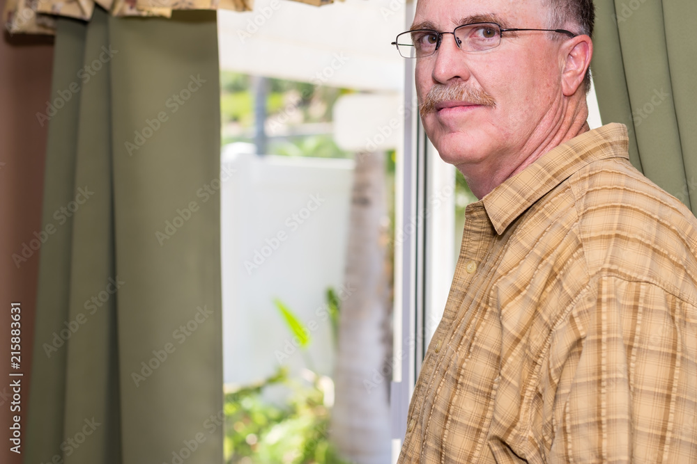 Serious older male portrait in kitchen at home with window to outside in background Serious older male portrait in kitchen at home with window to outside in background