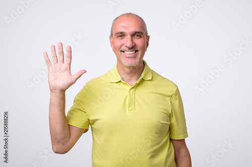 Friendly-looking attractive european man waiving hand in hello gesture while smiling cheerfully. Host is glad to welcome his guests or friends