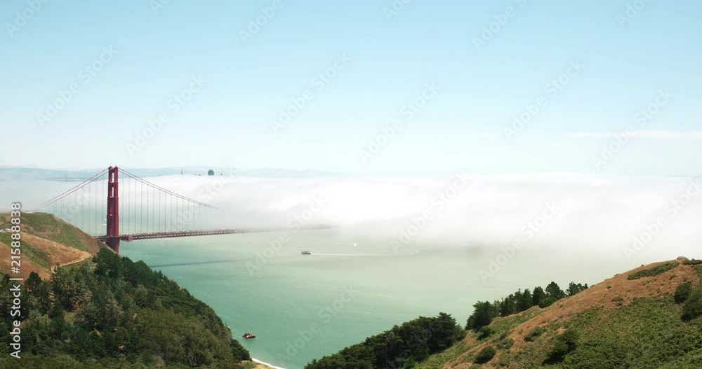 Summer fog flowing over the Golden Gate Bridge.  Viewed from above in the Marin Headlands.  Wide angle.  Mid-afternoon.  Blue sky above the fog.
