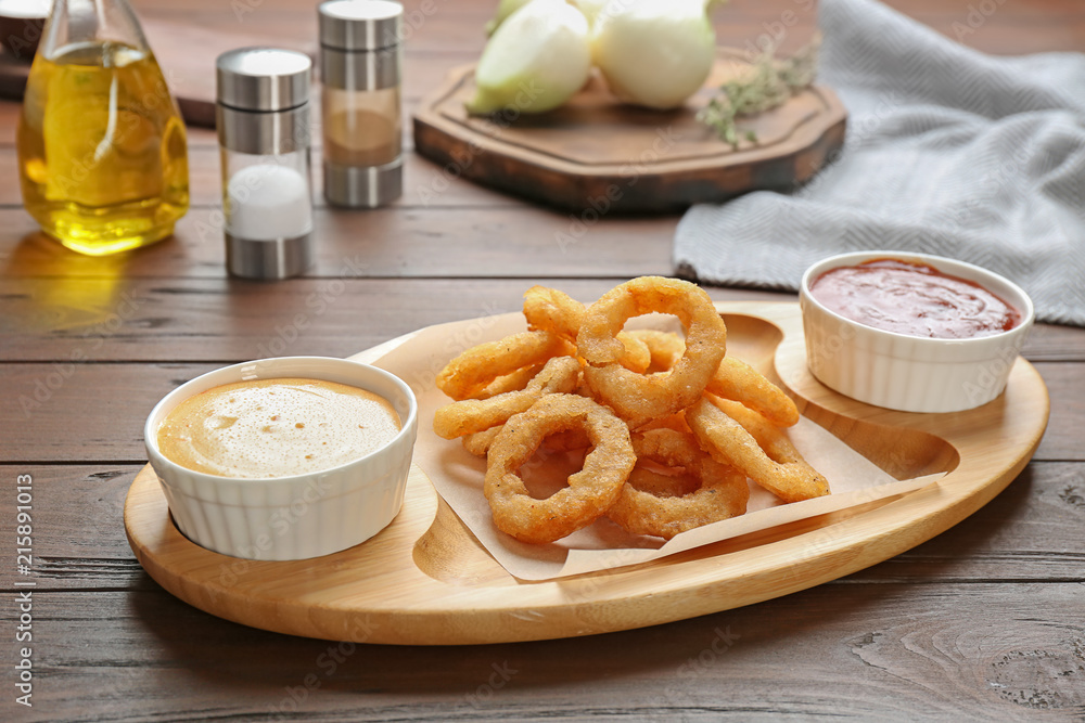 Plate with fried onion rings and sauces on table