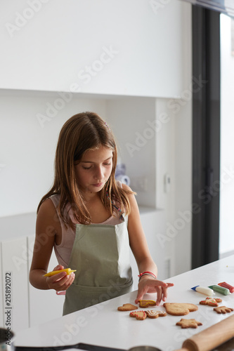 Little girl decorating homemade cookies in the kitchen