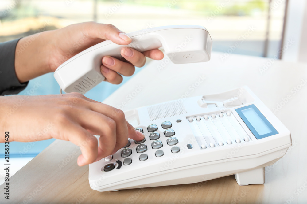 Woman dialing number on telephone at table in office Woman dialing number on telephone at table in office