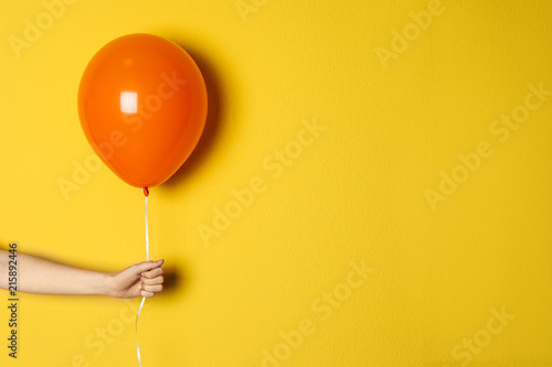 Woman holding orange balloon on color background