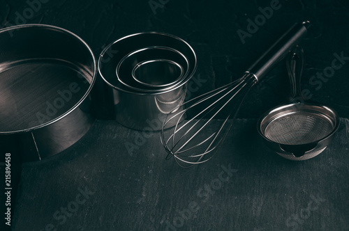 Ingredients and dishes on a black concrete table, where the corolla also lies, is filled with flour, three chicken eggs and a slate board. View from above. Place under the text. photo