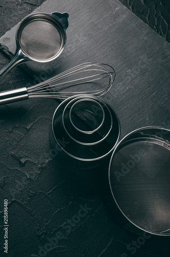 Ingredients and dishes on a black concrete table, where the corolla also lies, is filled with flour, three chicken eggs and a slate board. View from above. Place under the text.