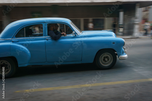 Habana, Cuba - 10 January, 2017:old blue car driving on a cuba street on a beautiful day with some people on the sidewalk
