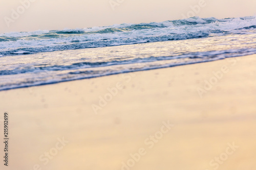 small wave coming to the beach and glassy fluffy white breaking wave on the sand with gold sunlight for background