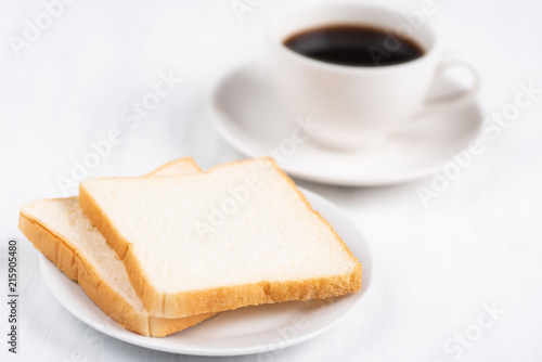 Sliced bread and cup of black coffee on white table, breakfast