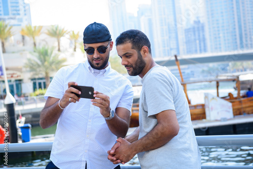Two friends looking at a smartphone and having fun at a marina in Dubai UAE