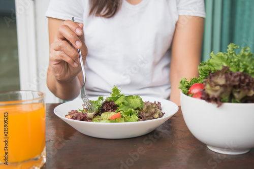 Eating healthy breakfast concept. woman holding dish of salad with variety vegetables and glass of orange juice on the floor in the morning at home.