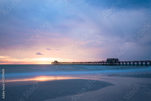Iconic Naples Pier the symbol of this famous city in southwest Florida, USA. Amazing and calm ocean during sunset, cloudscape after a big tropical storm in the Gulf of Mexico, close to Everglades Nati